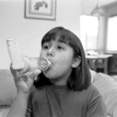 Young asthmatic girl using an inhaler attached to a spacer.